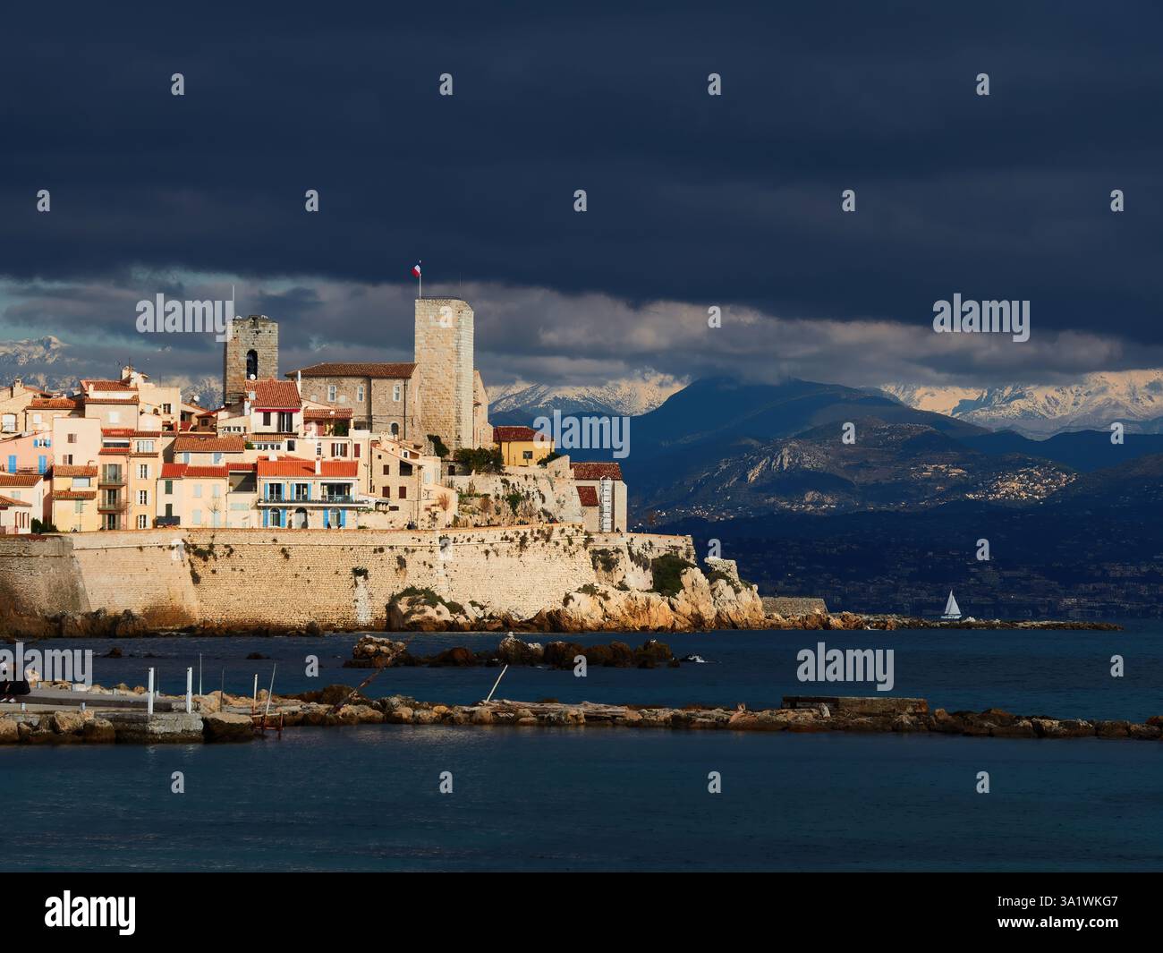 Die majestätische Küstenstadt Antibes unter dramatischem bewölktem Himmel und Bergkulisse Stockfoto
