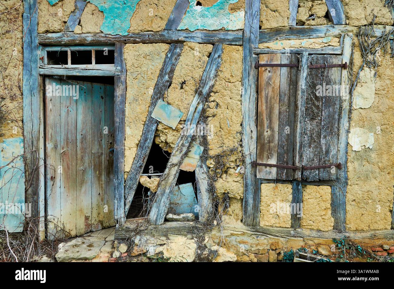 Alte verwitterte Hausmauer mit rustikaler Holztür und kaputtem Fenster Stockfoto