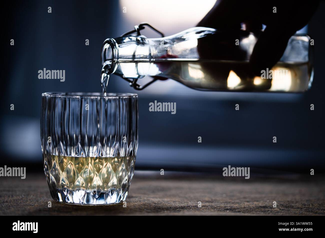 Ein Getränk aus einer durchsichtigen Flasche mit Schwenkdeckel in ein Glas in einem dunklen Raum gießen Stockfoto