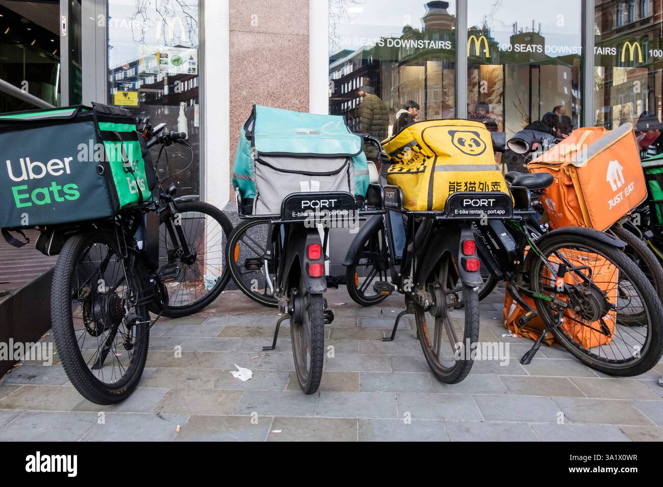 E-Bikes zur Lieferung von Mahlzeiten stehen vor einem McDonalds Restaurant, während Kuriere warten, um Essensbestellungen abzuholen. London Großbritannien. Stockfoto