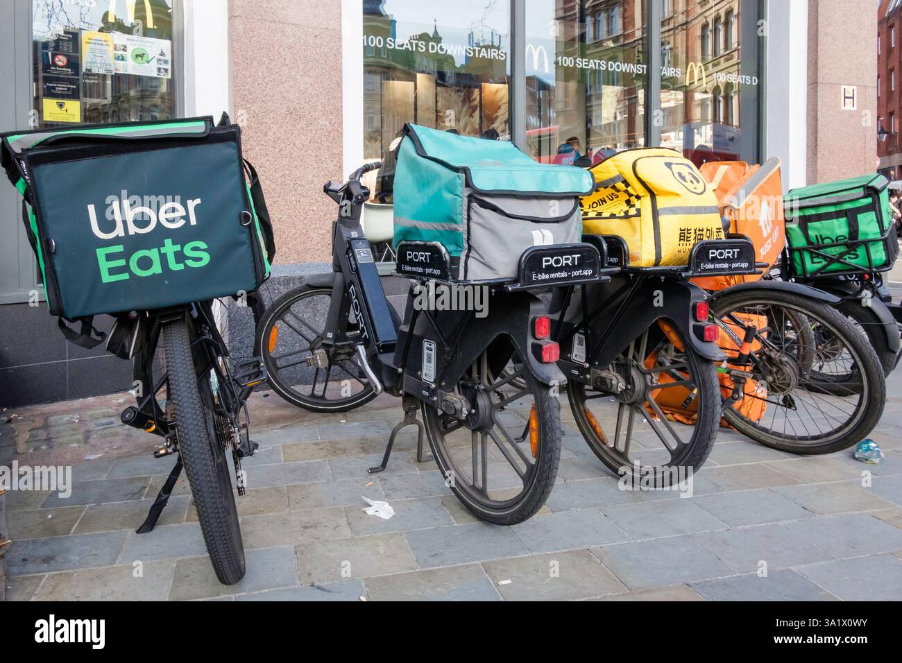 E-Bikes zur Lieferung von Mahlzeiten stehen vor einem McDonalds Restaurant, während Kuriere warten, um Essensbestellungen abzuholen. London Großbritannien. Stockfoto