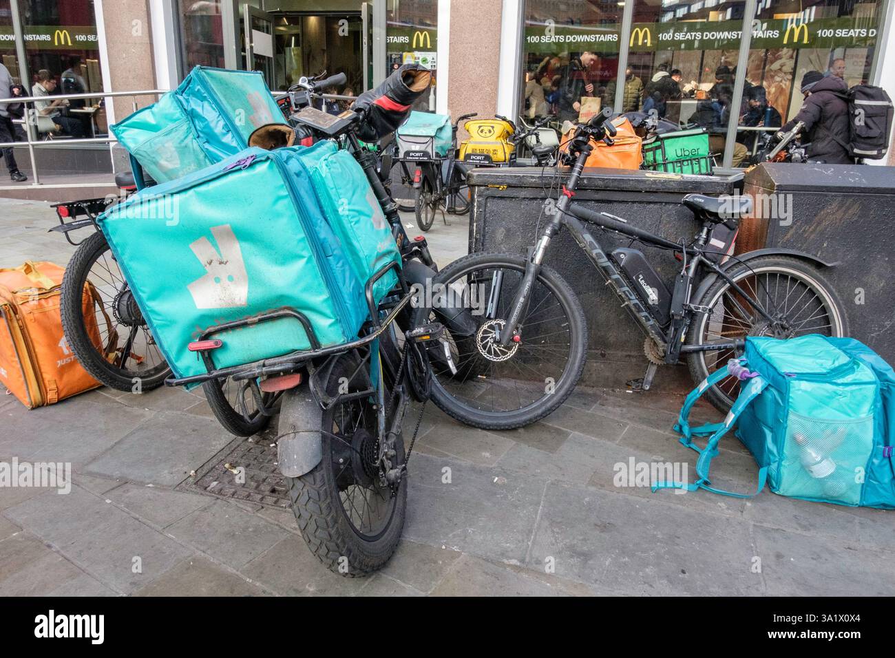 E-Bikes zur Lieferung von Mahlzeiten stehen vor einem McDonalds Restaurant, während Kuriere warten, um Essensbestellungen abzuholen. London Großbritannien. Stockfoto