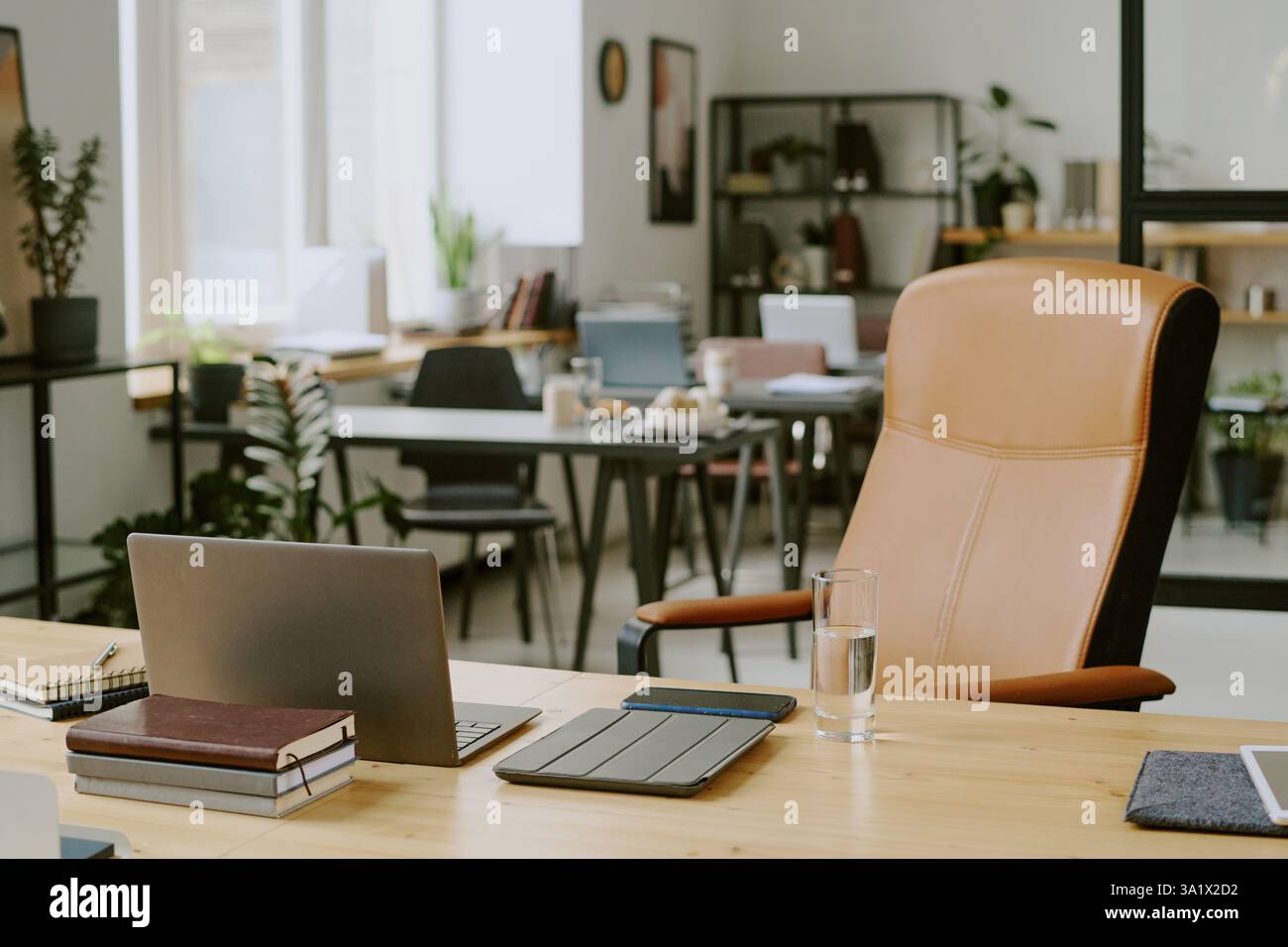 Holzschreibtisch mit Laptop und Büroartikeln auf der Oberseite und beigefarbener Ledercomputerstuhl im modernen Büro Stockfoto