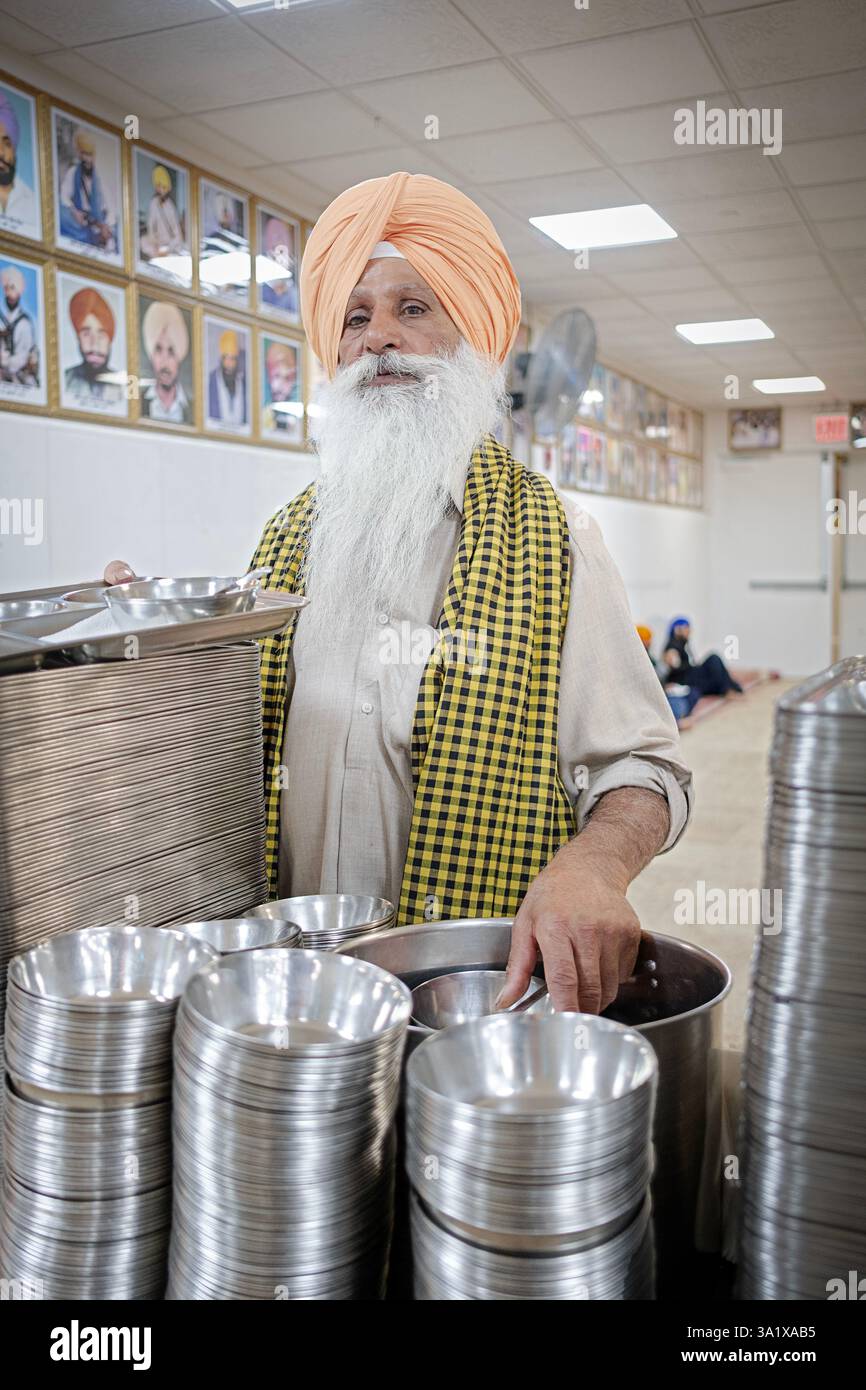Ein älterer Sikh-Mann mit einem langen weißen Bart überreicht den Besuchern des Langars des Tempels Tabletts und Schüsseln, ein Ort, an dem kostenlose Speisen für alle verfügbar sind. Stockfoto