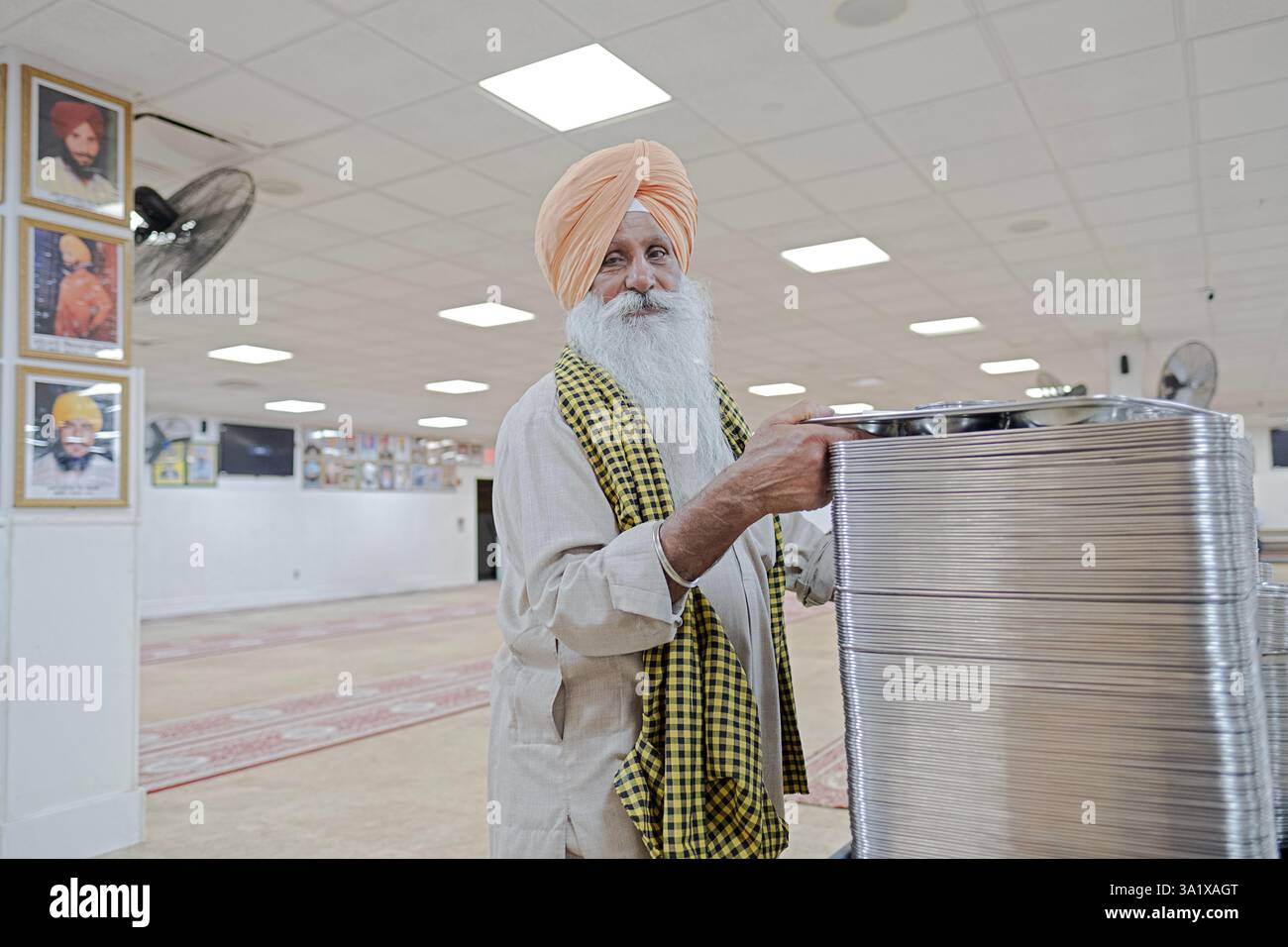 Ein älterer Sikh-Mann mit einem langen weißen Bart überreicht den Besuchern des Langars des Tempels Tabletts und Schüsseln, ein Ort, an dem kostenlose Speisen für alle verfügbar sind. Stockfoto