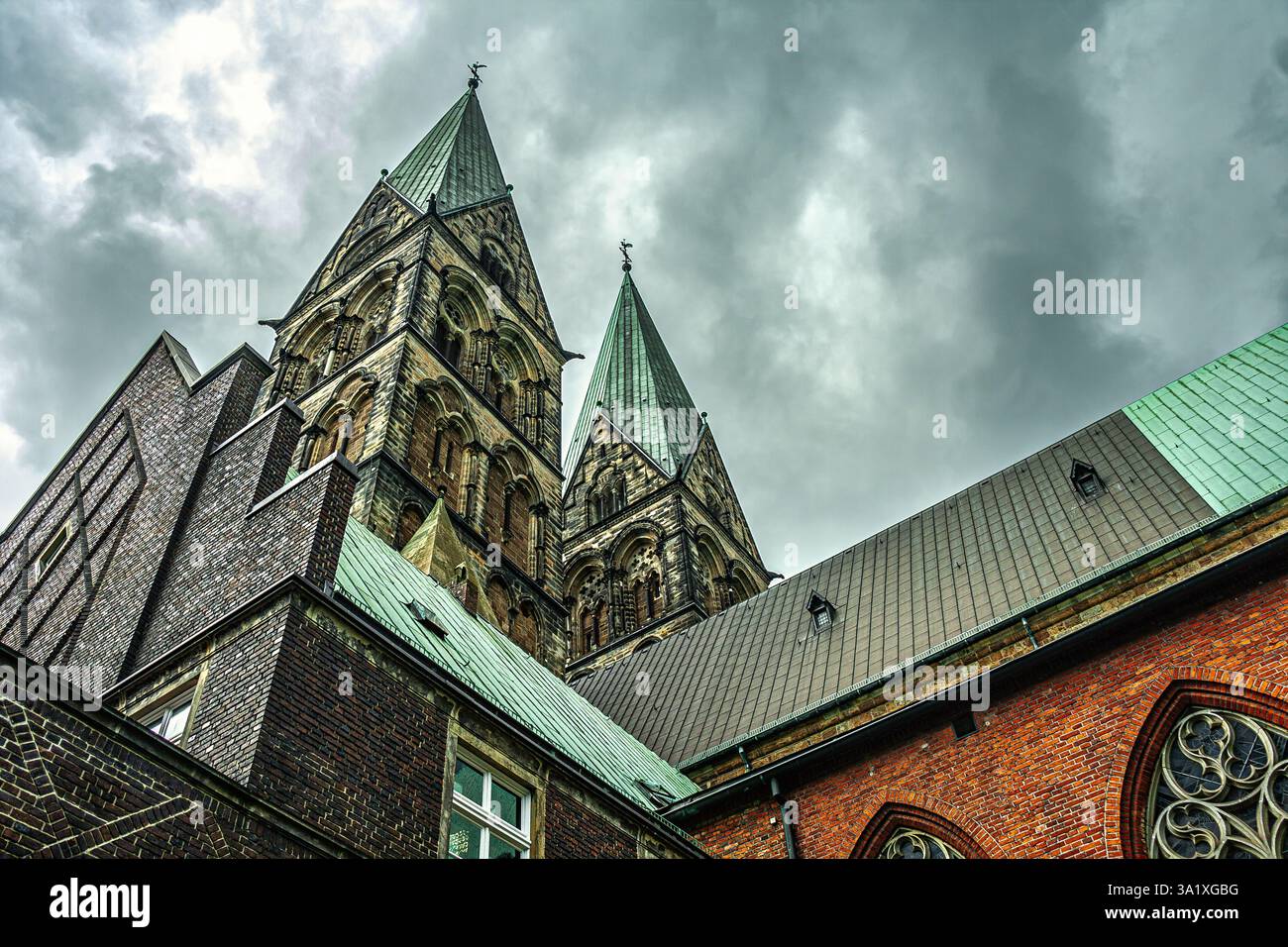 Flacher Blick auf die majestätischen Steintürme und Bronzedächer des Bremer Doms, die sich dramatisch vor einer bewölkten Kulisse erheben. Bremen, Deutschland Stockfoto