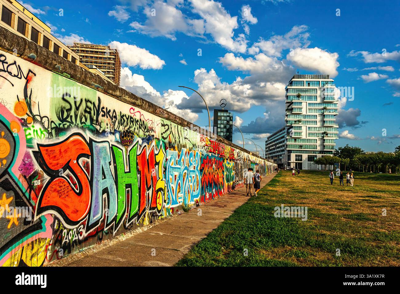 Farbenfrohe Graffiti auf dem East Side Gallery Abschnitt der Berliner Mauer mit Touristen, die die historische Stätte und Kunstwerke bewundern. Berlin Stockfoto