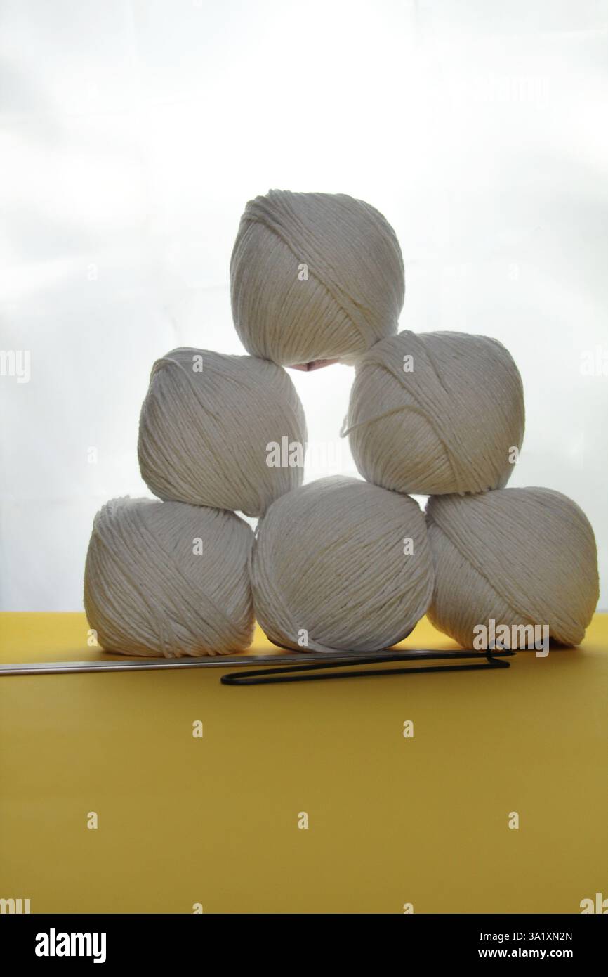 Weißes Garn in Form einer Pyramide wird durch weißes Licht beleuchtet. Strickzubehör liegt in der Nähe Stockfoto