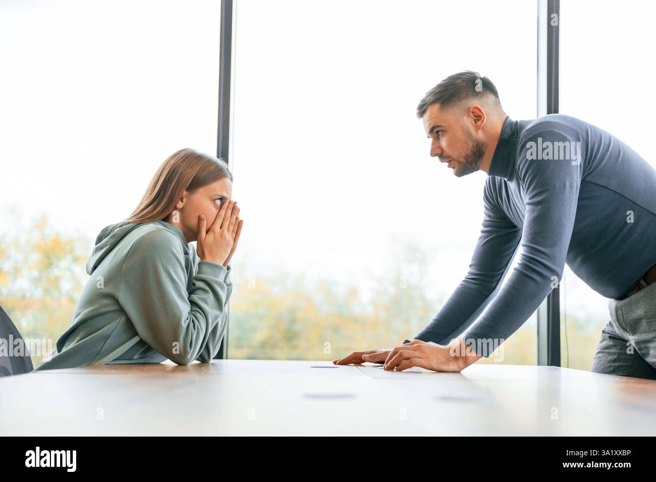 Seitenansicht, in der Nähe eines großen Fensters. Der Mann schreit seine Freundin an, Vorstellung von Streit. Stockfoto