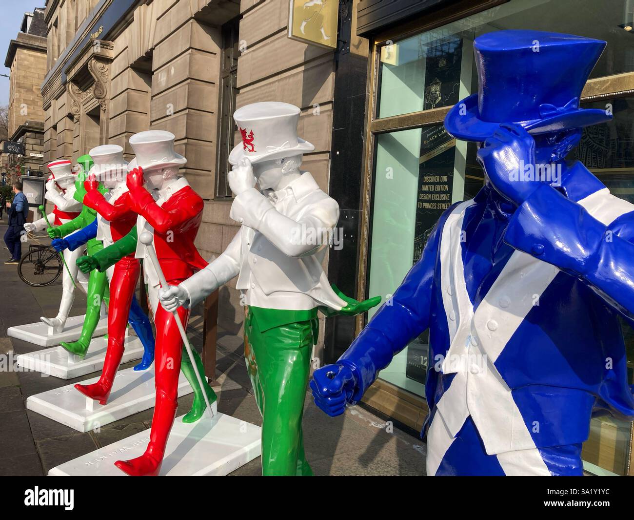 Johnnie Walker Whisky Striding man Statuen in Six Nations Rugby Farben außerhalb der Johnnie Walker Experience, Hope Street, Edinburgh Schottland, 2025 - Smartphone-aufgenommenes Stockfoto
