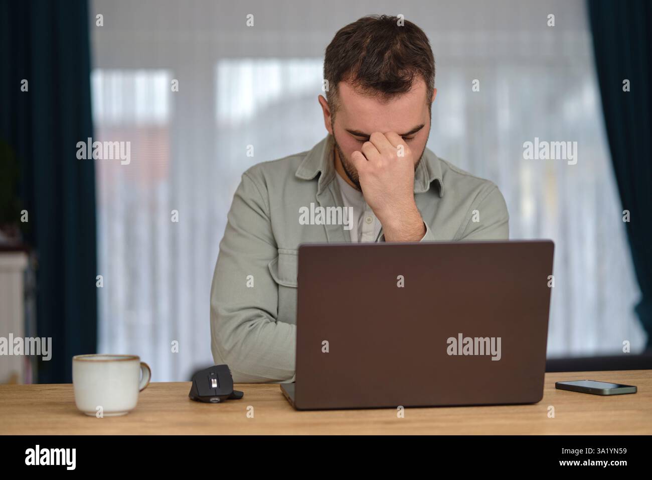 Ein müder Mann arbeitete Überstunden, saß am Schreibtisch vor einem Laptop und reibte sich die Augen mit den Händen. Stockfoto