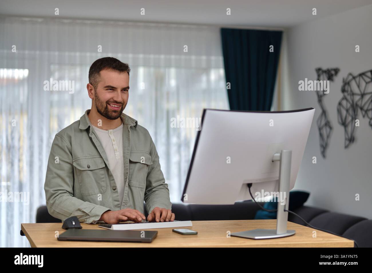 Ein glücklicher Mann, der einen Desktop-Computer benutzt, während er zu Hause arbeitet. Stockfoto