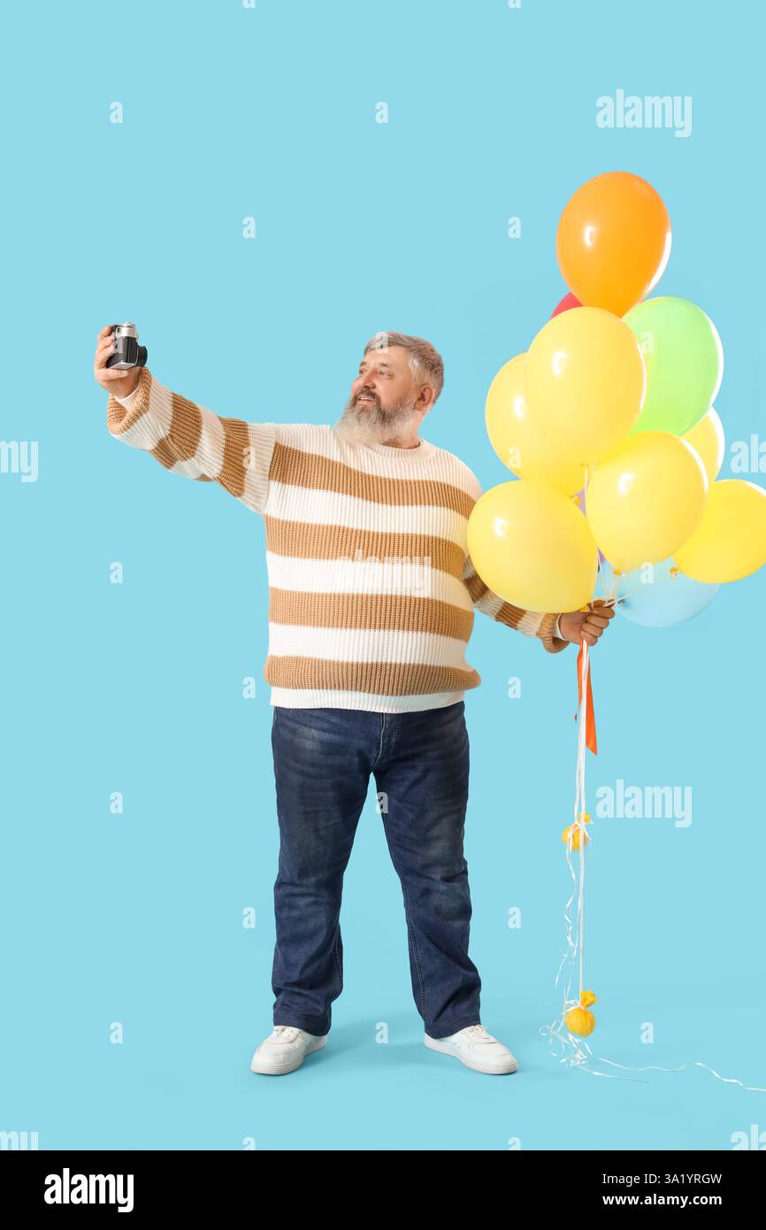 Senior Mann mit Ballons und Fotokamera, die Selfie auf blauem Hintergrund macht Stockfoto