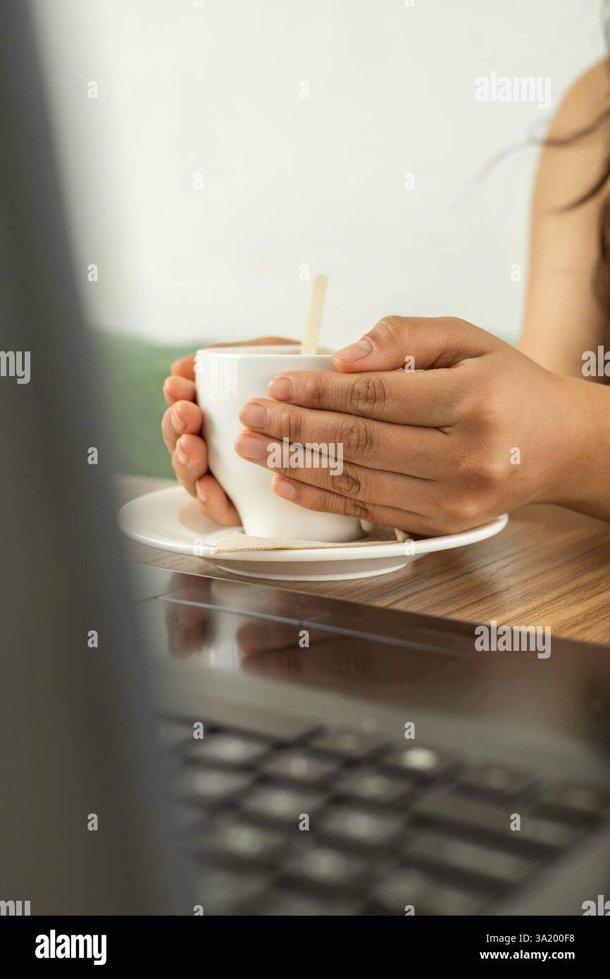 Ein süßer, gemütlicher Moment, in dem sich die Hände um eine warme Tasse cremiger heißer Schokolade wickeln und die wohlige Wärme und einfache Freude in einer zarten, heimeligen Umgebung genießen Stockfoto