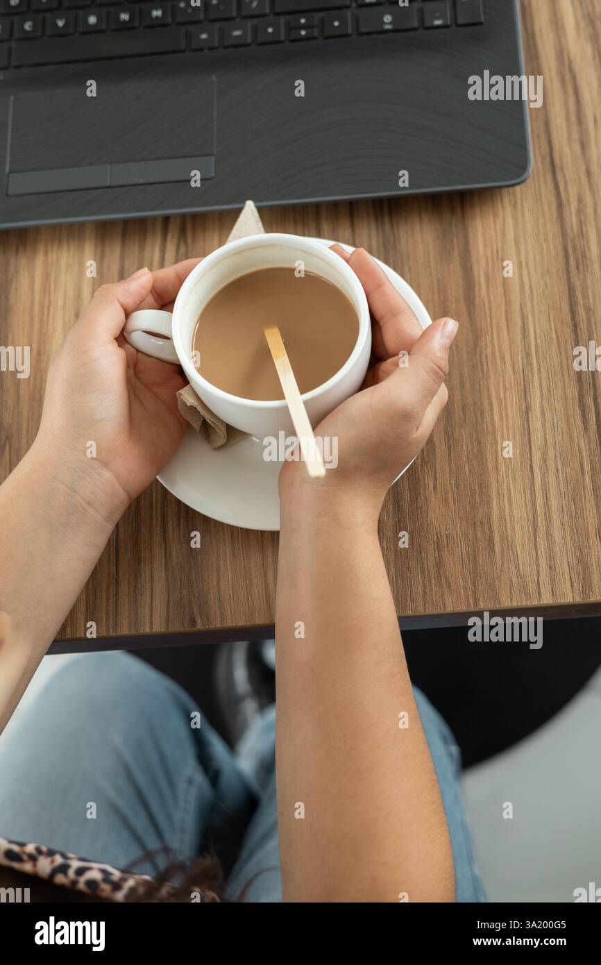 Ein moderner und ästhetischer Moment, in dem sich die Hände sanft um eine elegante, stilvolle Tasse cremiger heißer Schokolade wickeln und die Wärme und den verwöhnenden Geschmack eines genießen Stockfoto