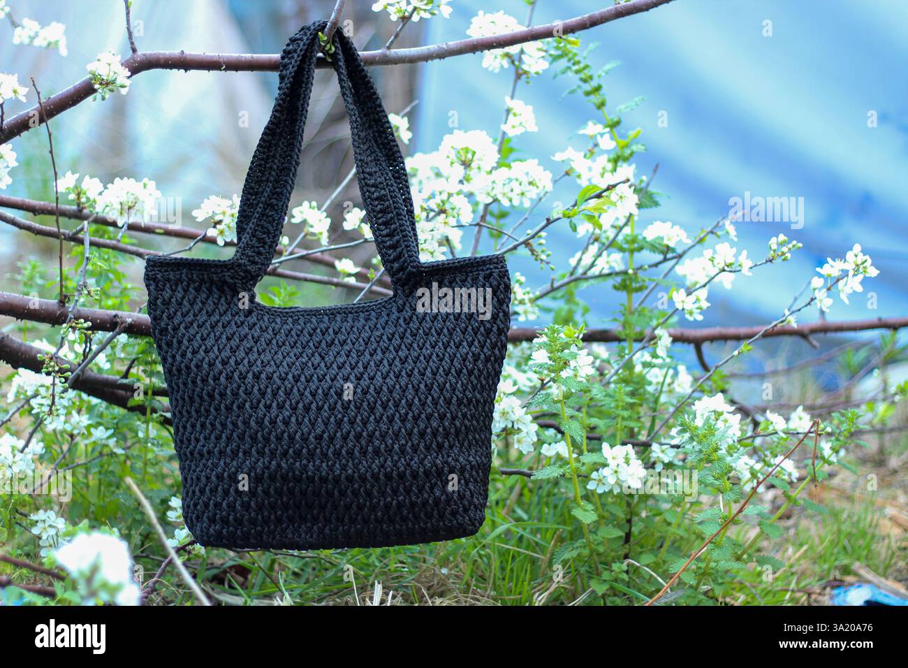 Gehäkelte schwarze Tasche, die am Pflaumenzweig im Garten hängt. Selektiver Fokus. Stockfoto