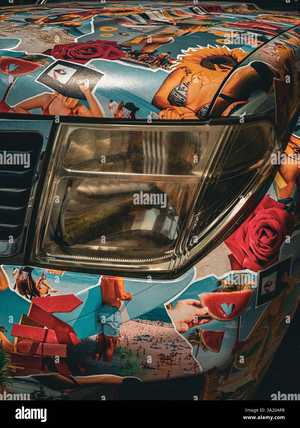 Pop-Art-Auto mit exzentrischem Collage-Design Eine Nahaufnahme der Vorderseite eines Fahrzeugs, die komplett mit farbenfroher, eklektischer Collage-Kunst bedeckt ist. Die lebendige Ästhetik - Smartphone-aufgenommenes Stockfoto
