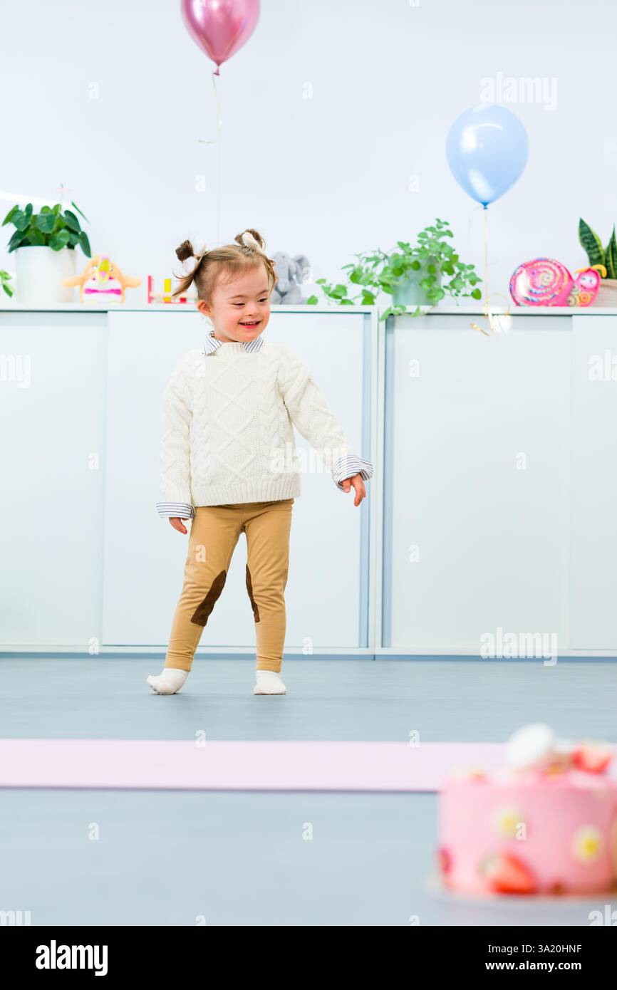 Niedliches 3-jähriges Mädchen mit Down-Syndrom feiert ihren Geburtstag in einem mit Ballons dekorierten Spielzimmer. Kindergeburtstag. Stockfoto