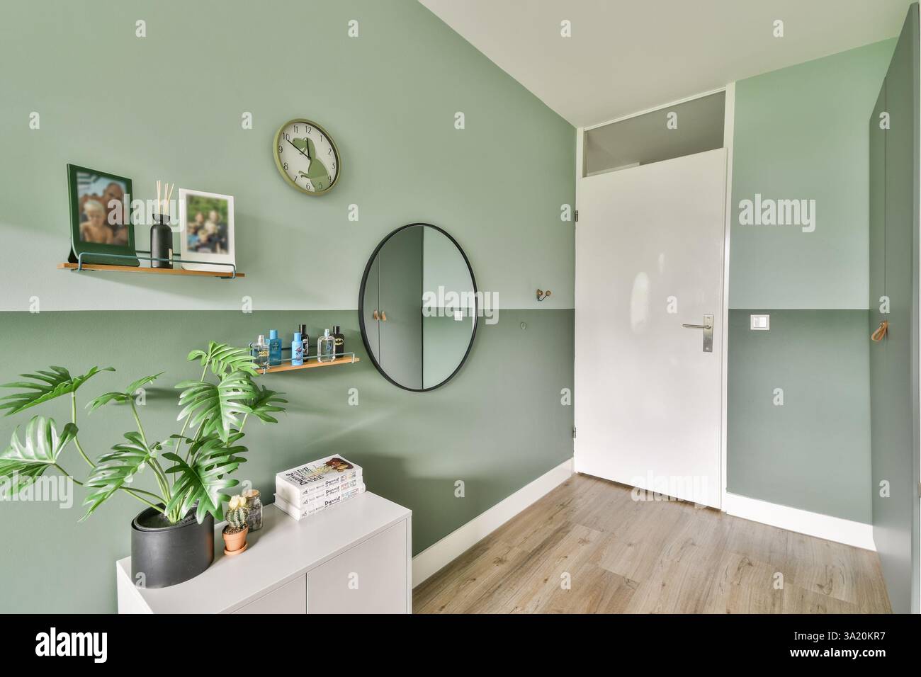 Die moderne Inneneinrichtung mit einer ruhigen grünen Wand, minimalistischer Einrichtung und einem stilvollen Spiegel spiegelt moderne Designtrends wider. Stockfoto