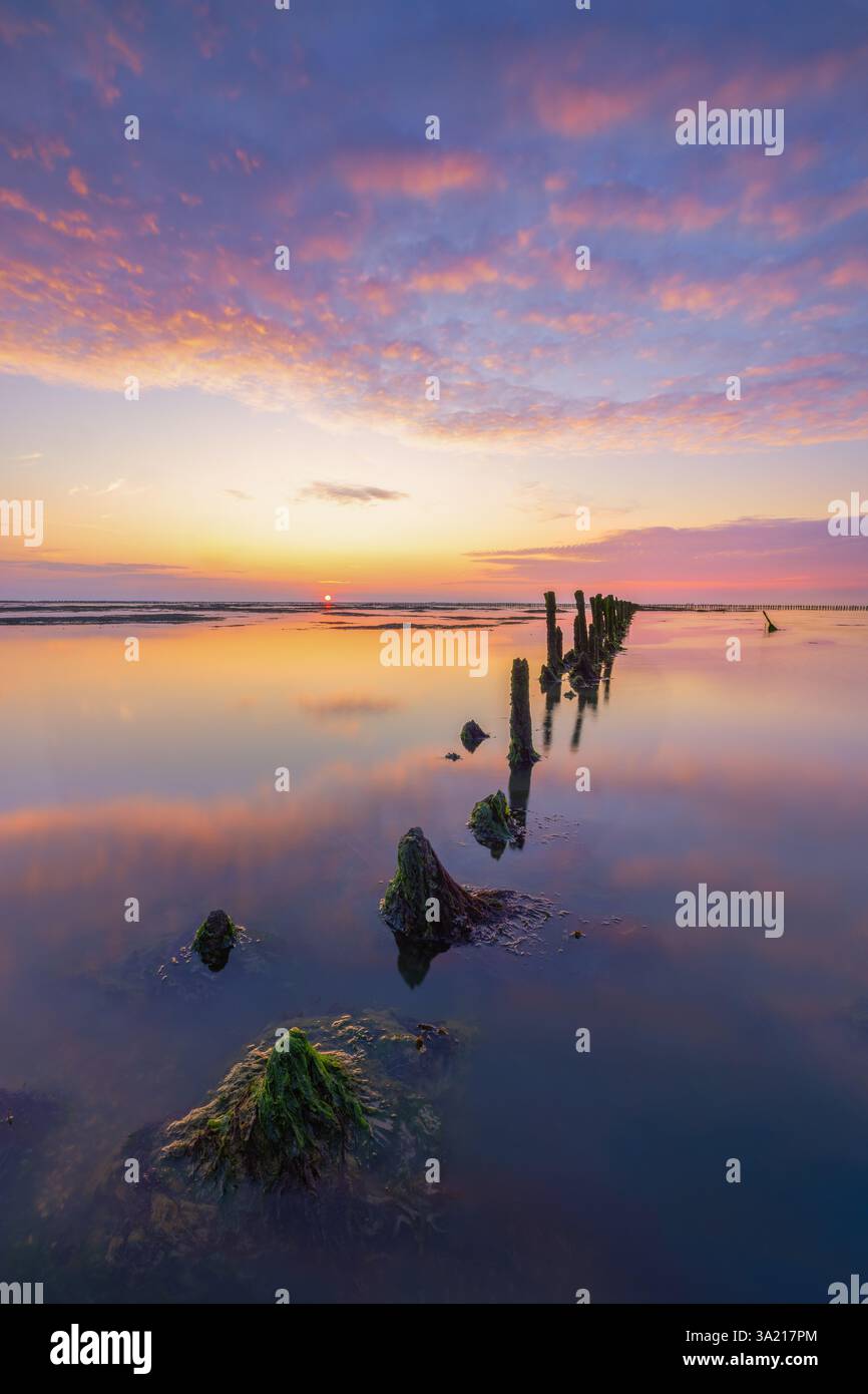 Ein wunderschöner Sonnenuntergang über dem Wattenmeer mit einem Himmel voller Abendrot. Die Farben spiegeln sich auf dem Wasser des Meeres wider. - Meeresbild Stockfoto