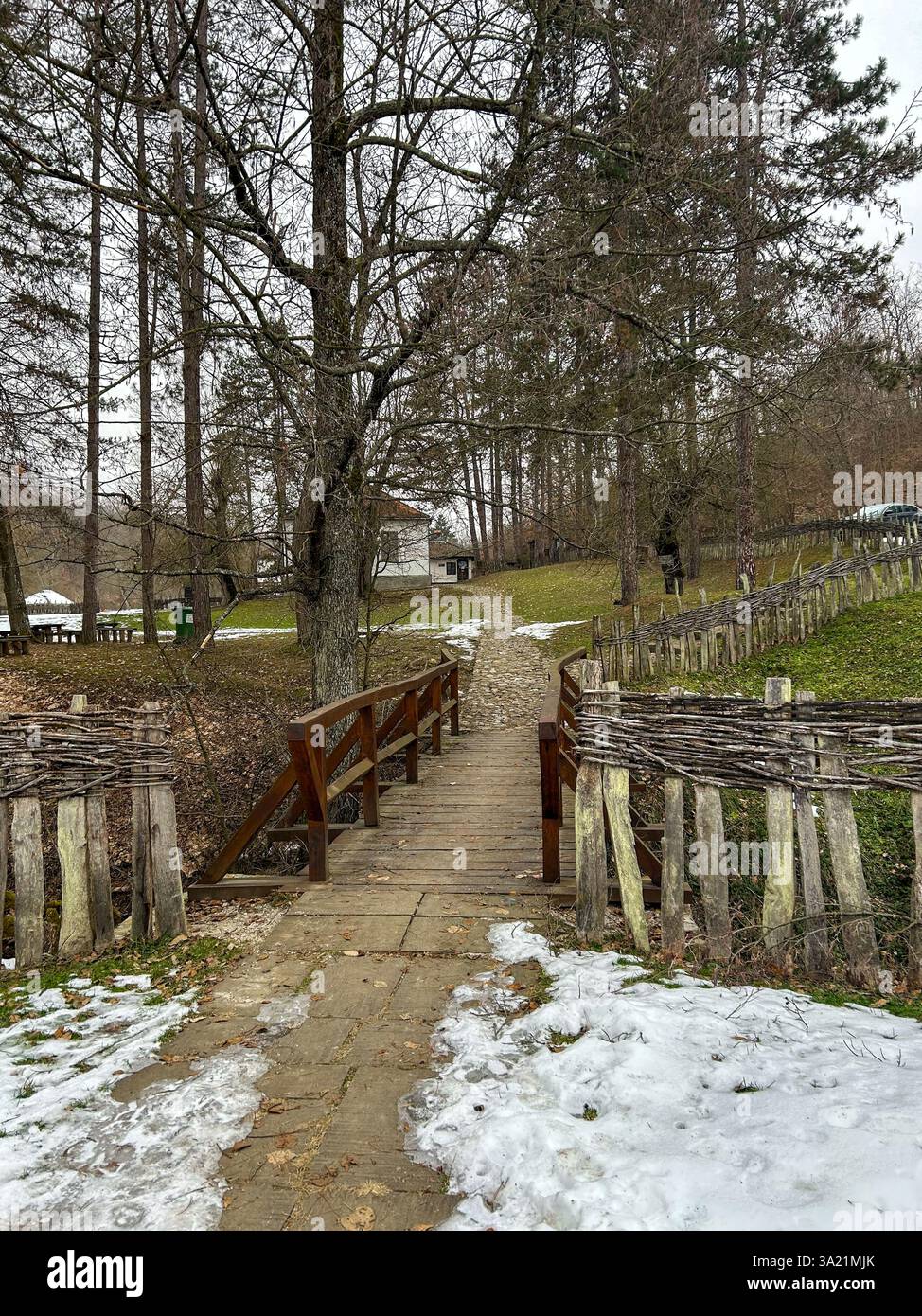 Eine bezaubernde Holzbrücke mit Schnee, eingebettet in ein traditionelles serbisches Dorf, die die friedliche Schönheit des Winters und des Kulturerbes einfängt - Smartphone-aufgenommenes Stockfoto