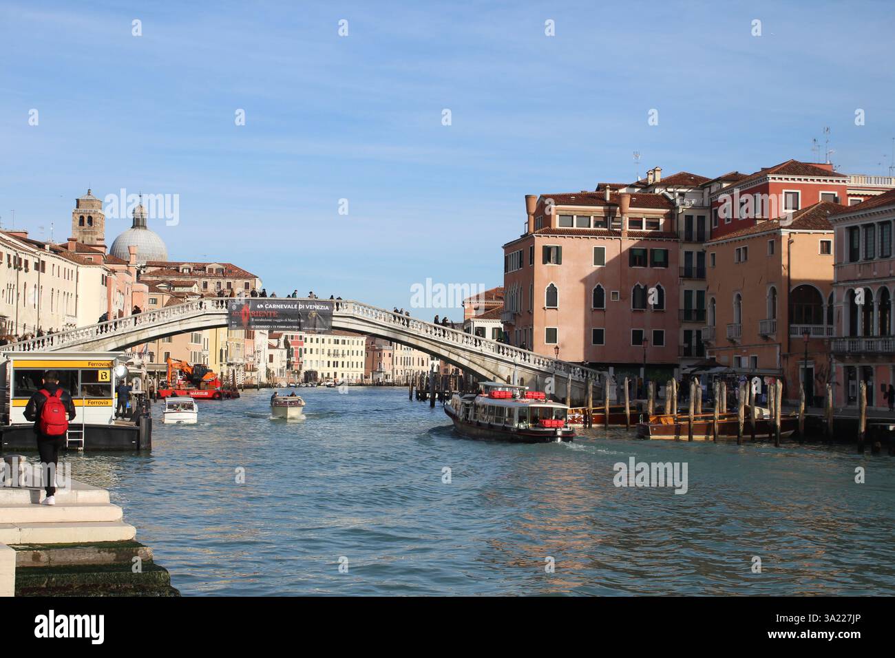Heller Wintertag in Venedig: Ein malerischer Kanal mit Booten, eine bezaubernde Brücke und farbenfrohe historische Gebäude unter klarem blauem Himmel. Stockfoto