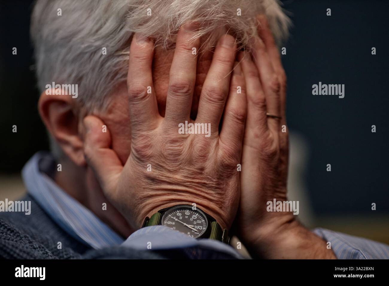 Ältere Menschen halten das Gesicht in den Händen, zeigen Armbanduhr und tragen einen Pullover, was eine Atmosphäre der Besinnung und Privatsphäre schafft Stockfoto
