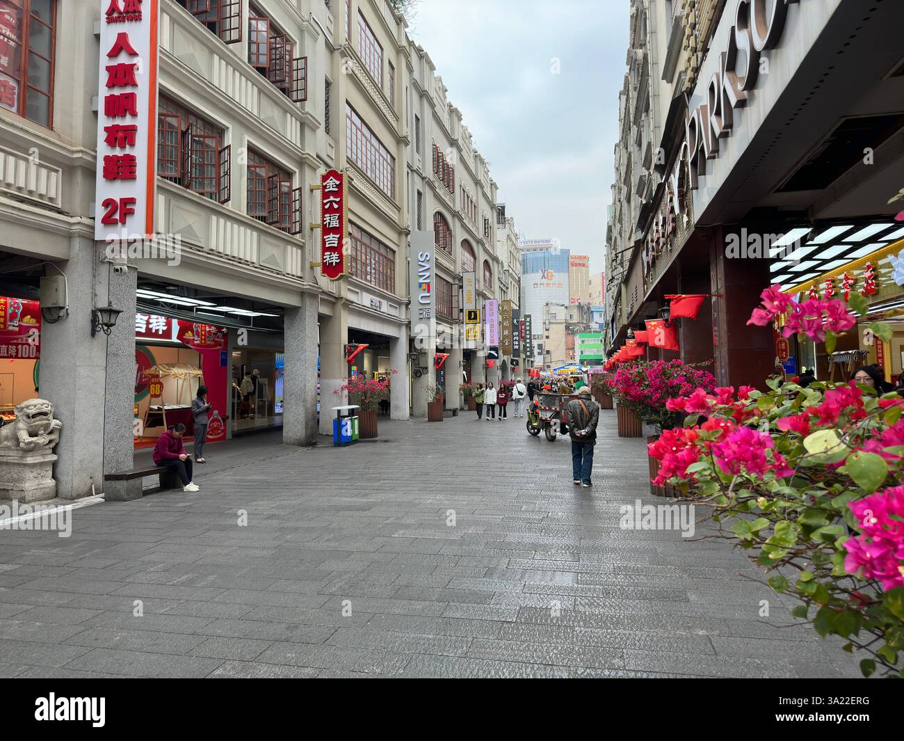 Nanning, Guangxi, China - 2. Dezember 2023: Straßenscen in einer chinesischen Stadt, gesäumt von Geschäften und lebendigen Blumen. - Smartphone-aufgenommenes Stockfoto