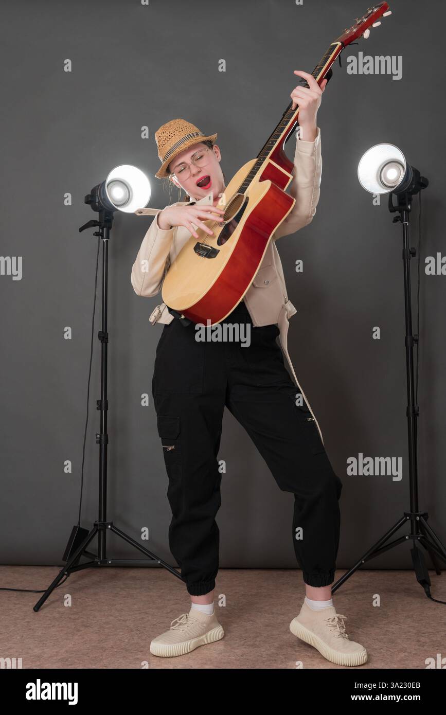 Ausdrucksstarke Gitarristin und Sängerin Songwriterin spielt klassische Gitarre und singt Lied mit geschlossenen Augen und steht in voller Länge auf der Bühne. Verspielter Mus Stockfoto