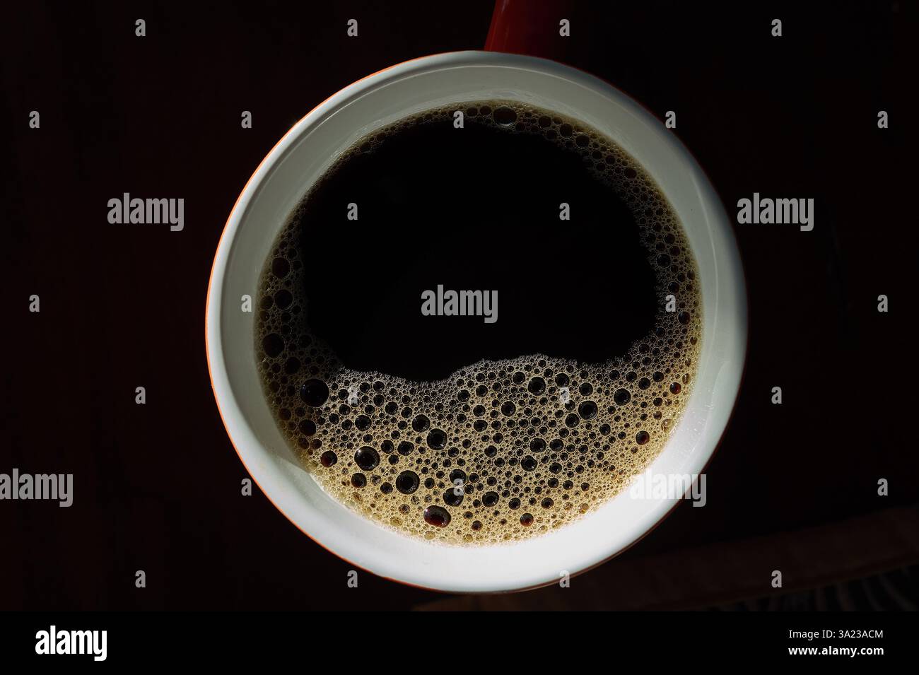 Blick von oben auf eine weiße Kaffeetasse gefüllt mit schwarzem Kaffee, üppigen Blasen und Schaum, dunkler Hintergrund. Minimalistisches Koffeinkonzept, Morgenenergie Stockfoto