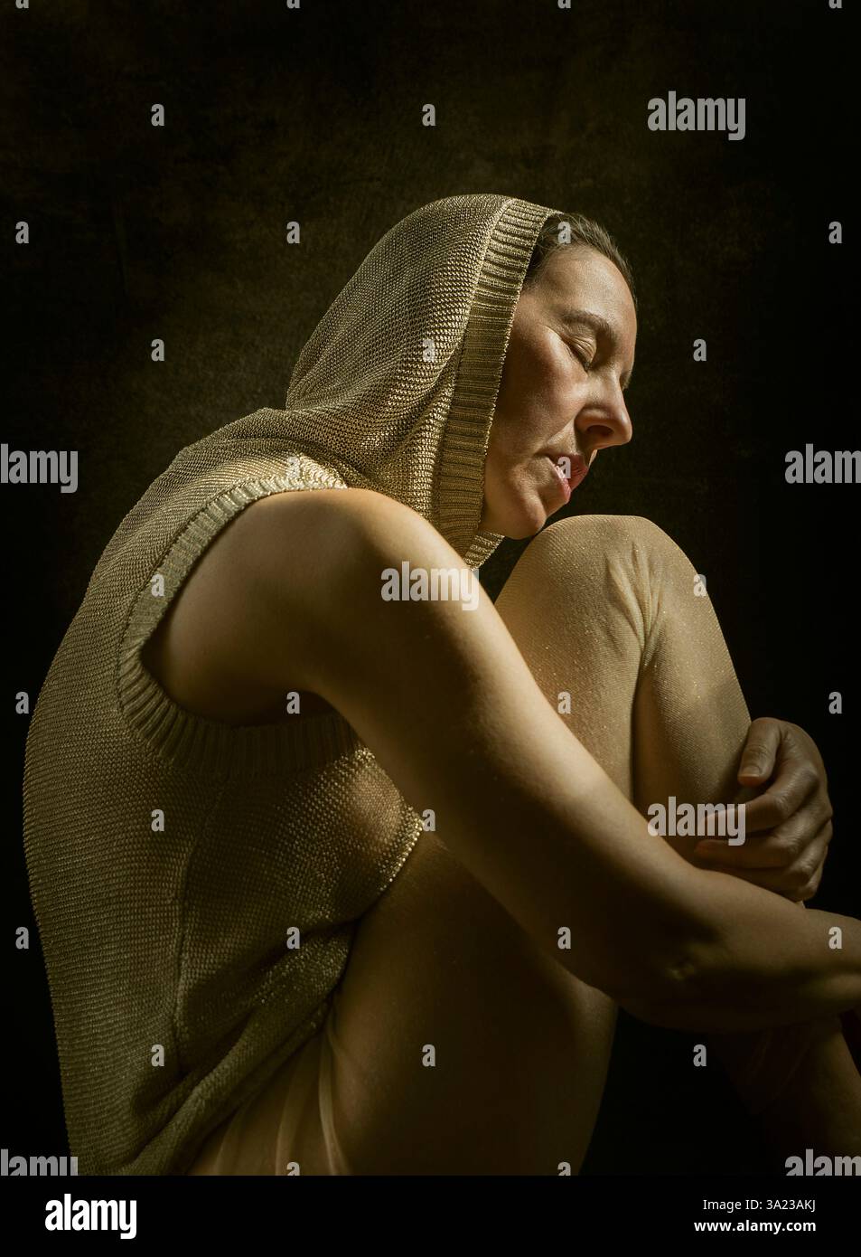 Frau mit goldener Kapuze sitzt und über ihre Arme schaut, die auf ihren Beinen liegen 6, spanien Stockfoto
