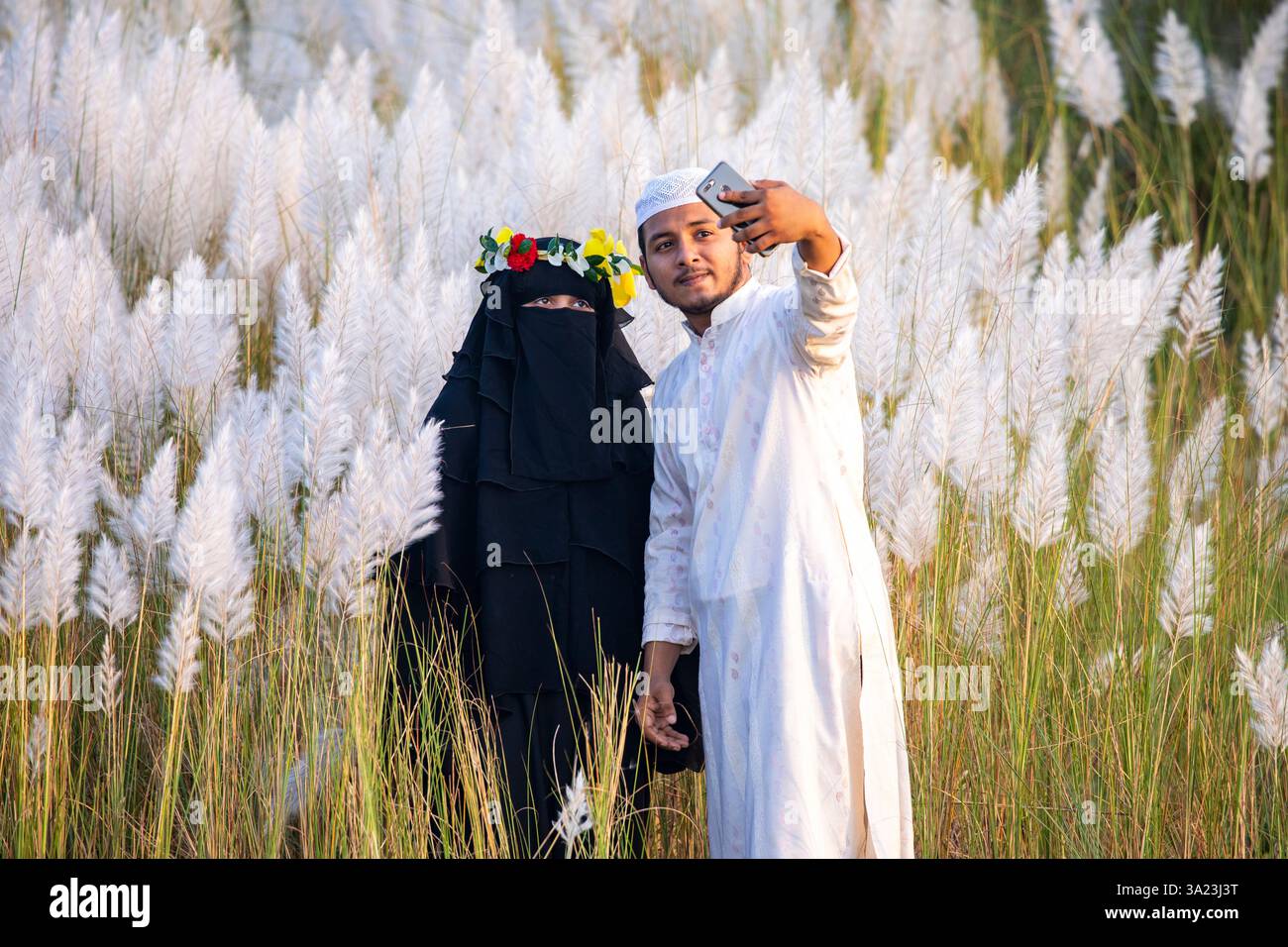 Ein muslimisches Paar, das in die Schönheit der blühenden Kans-Grasblumen eintaucht und das Wesen des Herbstes am Stadtrand von Dhaka, Bangla, feiert Stockfoto