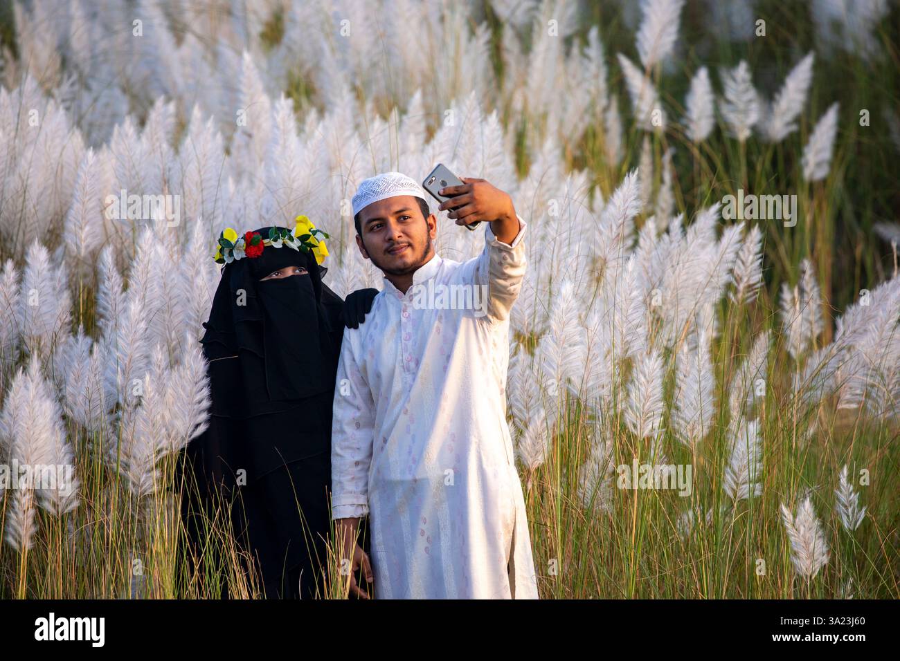 Ein muslimisches Paar, das in die Schönheit der blühenden Kans-Grasblumen eintaucht und das Wesen des Herbstes am Stadtrand von Dhaka, Bangla, feiert Stockfoto