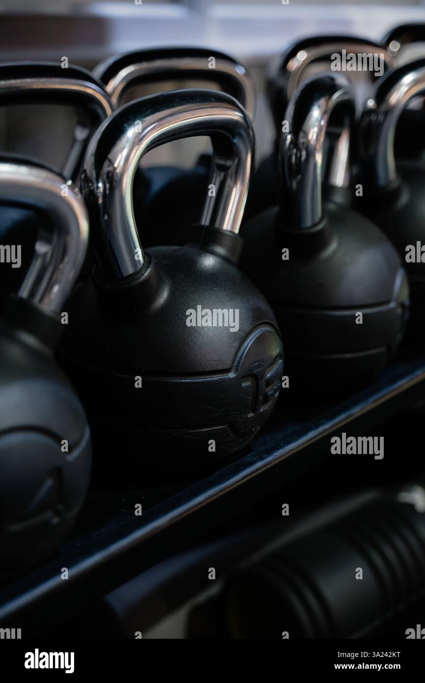 Eine Reihe schwarzer Kettlebells befindet sich auf einem Regal. Die Wasserkocher haben alle verschiedene Größen und sind alle schwarz Stockfoto