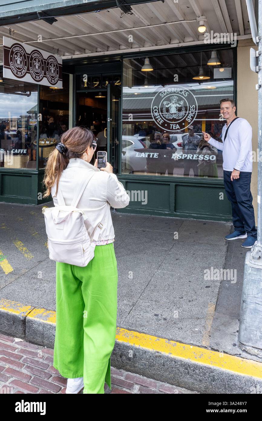 Ein Tourist macht ein Foto von einem Mann, der auf das ursprüngliche Starbucks in Seattle, WA zeigt. Sie besuchen das berühmte Wahrzeichen. Stockfoto