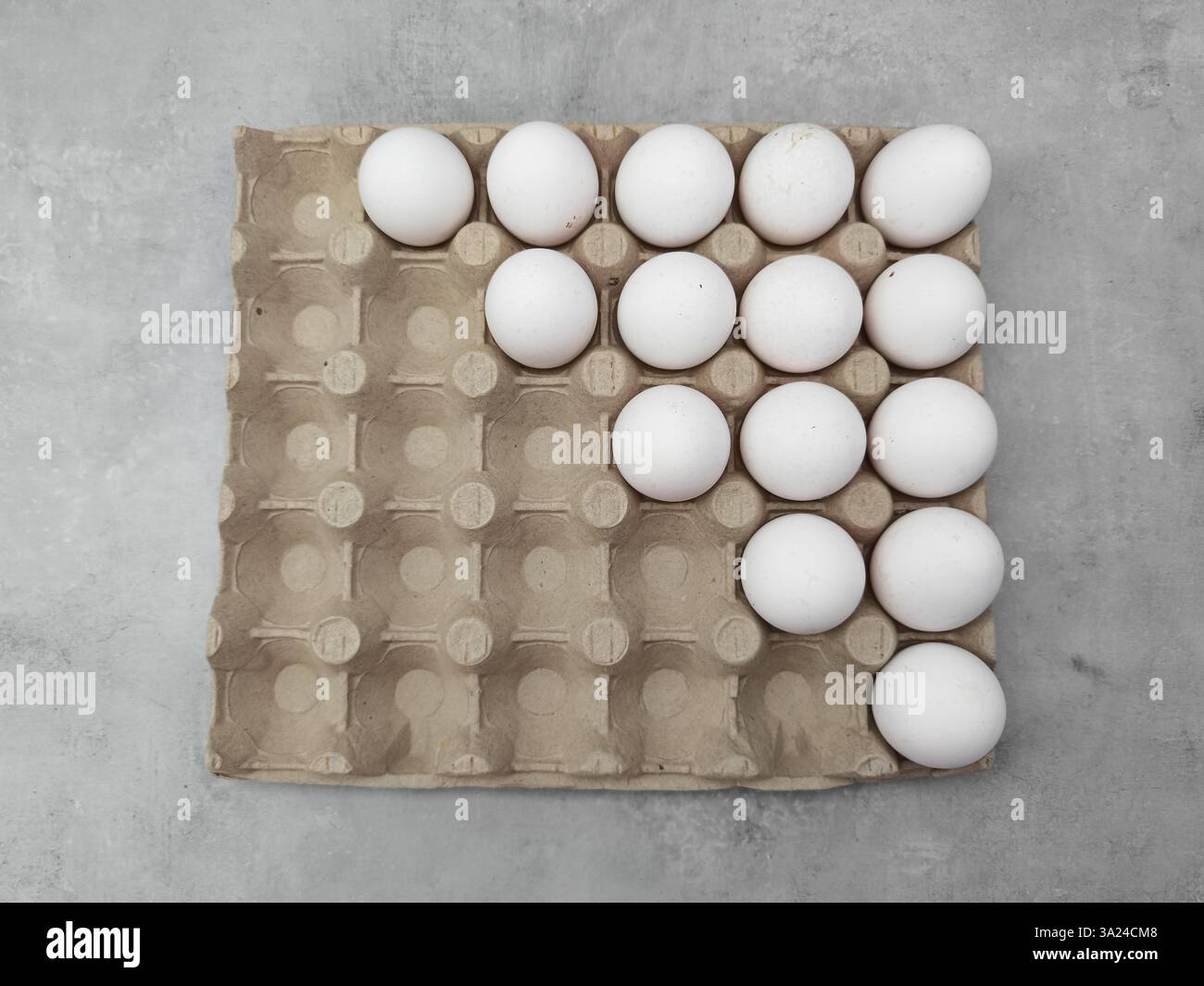 Weiße Eier, die eine Pfeilform im Karton auf grauem Hintergrund bilden ostern Stockfoto