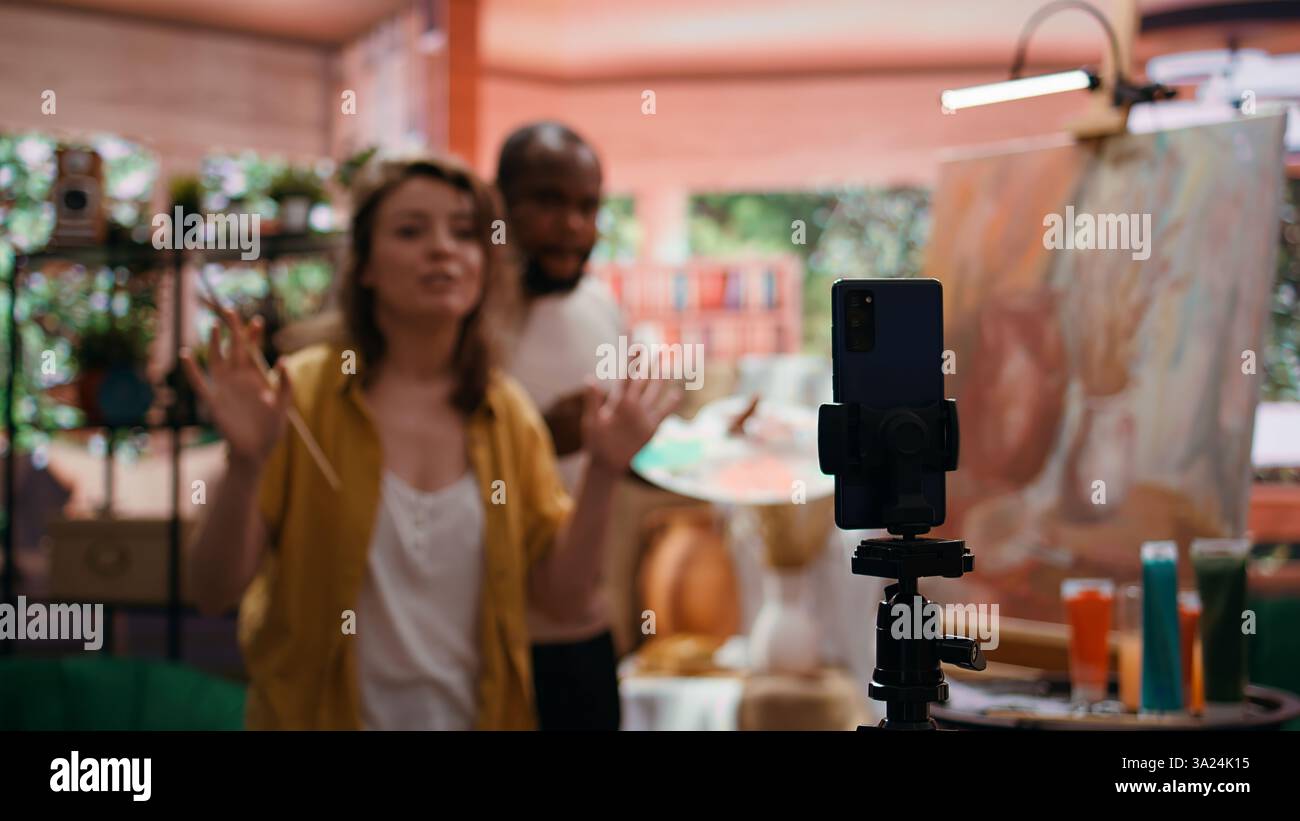 Frau Künstlerin moderiert Online-Kurs, um Produkte und Techniken zu präsentieren, die auf rustikalen Kunstwerken verwendet werden, und nimmt Tutorial online auf. Team von Malern, die Meisterklasse für E-Learning, Kunstunterricht machen. Kamera B.. Stockfoto