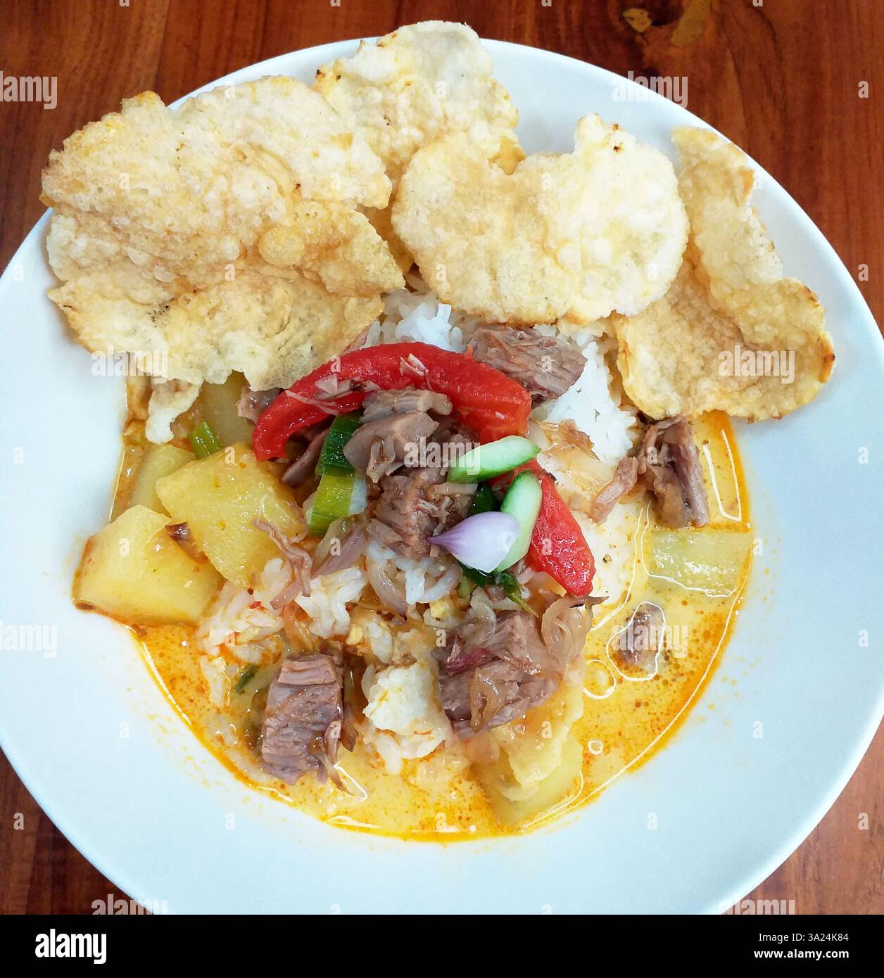 Indonesisches Essen: Soto Betawi, eine Suppe auf Kokosnussbasis mit kleinen Rindfleischstücken oder Schlachtnebenerzeugnissen, serviert mit Reis und leeren Crackern. Stockfoto