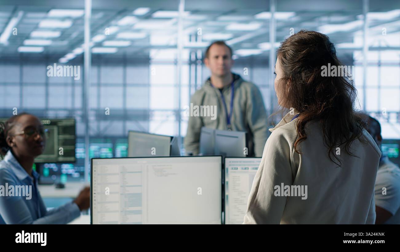 Manager, der den Serverraum beaufsichtigt, hält spontane Besprechungen mit Mitarbeitern ab. Vorgesetzter im Server-Hub, bittet um Aufmerksamkeit, den Mitarbeitern Feedback zu geben, nachdem die Inspektion durchgeführt wurde, Kamera A Stockfoto