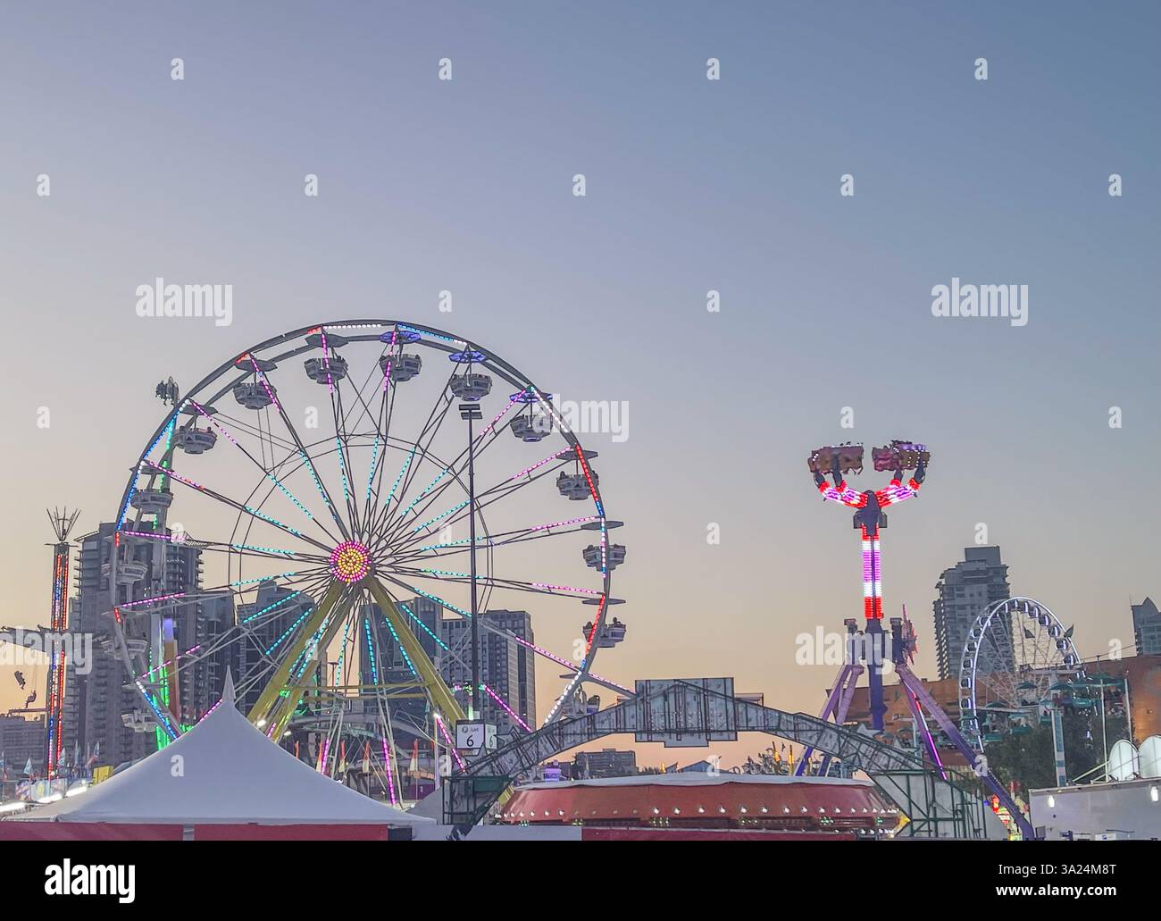 Beleuchtetes Riesenrad und Fahrten am Karneval in der Abenddämmerung Stockfoto