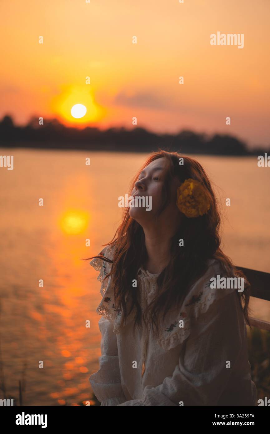 Ruhiger Sonnenuntergang am Seeufer mit einer Frau in traditioneller Kleidung, die Ruhe, natürliche Schönheit und landschaftlich reizvollen Charme verkörpert Stockfoto