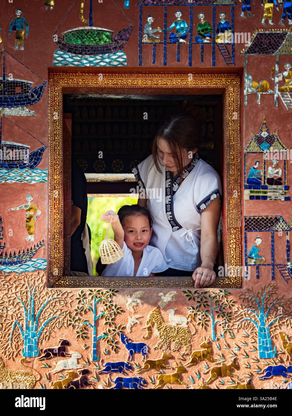 Mutter und Kind im Wat Xieng Thong, Luang Prabang, Laos. Traditionelle Kunst, Kulturfenster Stockfoto