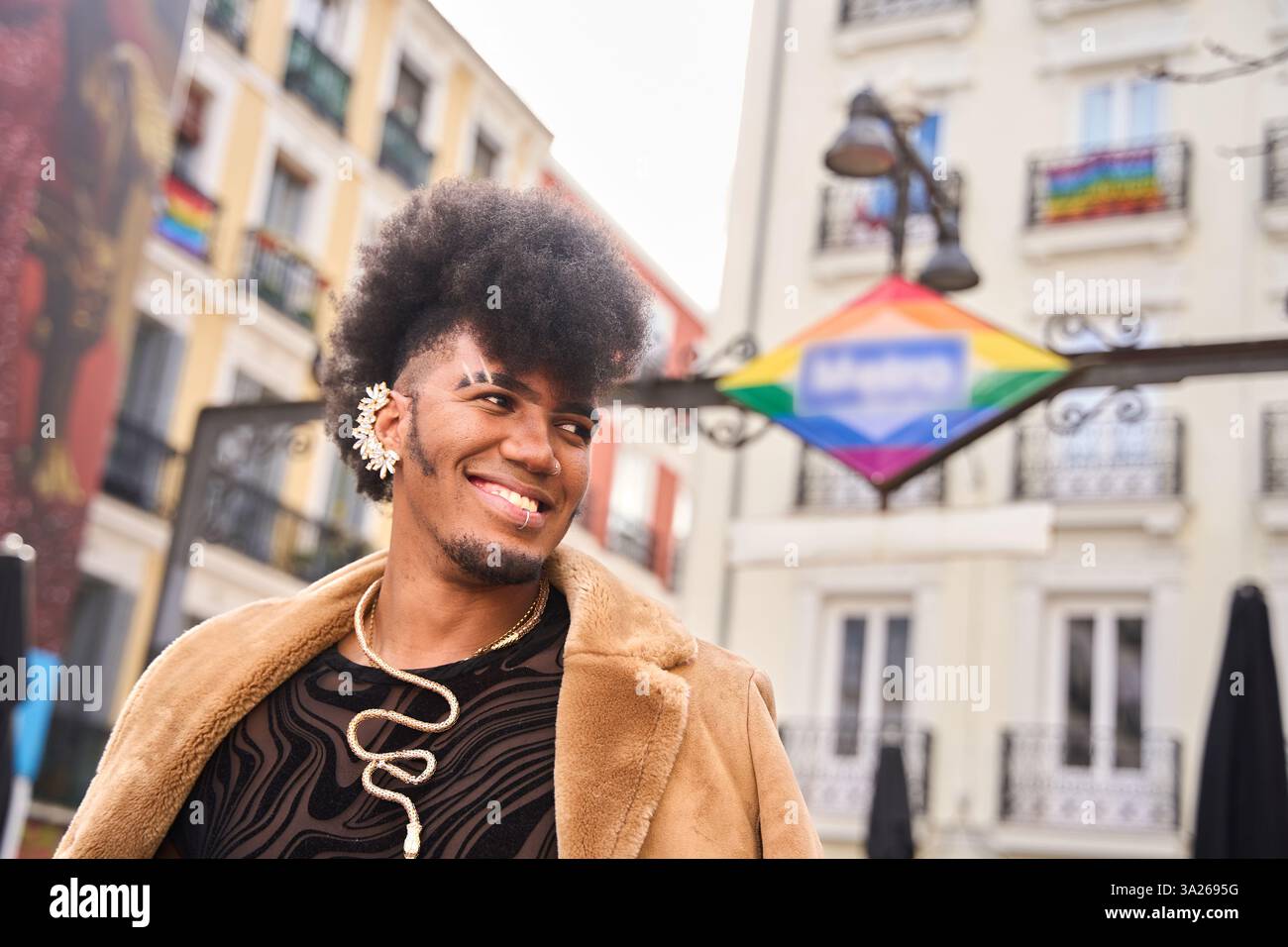 Porträt eines fröhlichen jungen androgynen Mannes mit Afro-Haaren mit Ohrring und Halskette, lächelnd in chueca, dem lgbtq und Madri Stockfoto