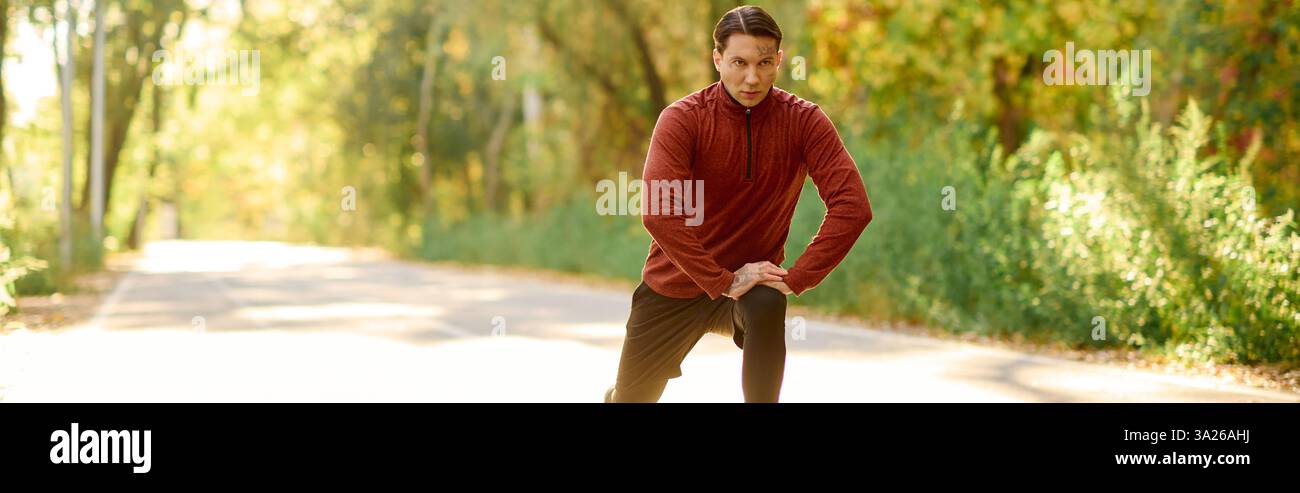 Selbstbewusster junger Mann mit Tätowierungen trifft eine modische Pose in einer lebhaften Outdoor-Umgebung. Stockfoto