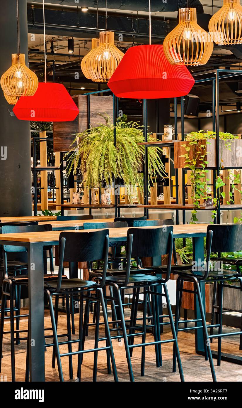Modernes Restaurant mit Holzmöbeln, Hängeleuchten und grünen Pflanzen – gemütlicher Speisesaal, modernes Café-Design, stilvolles Dekor, warme Atmosphäre, trendiges Urban Eatery Stockfoto