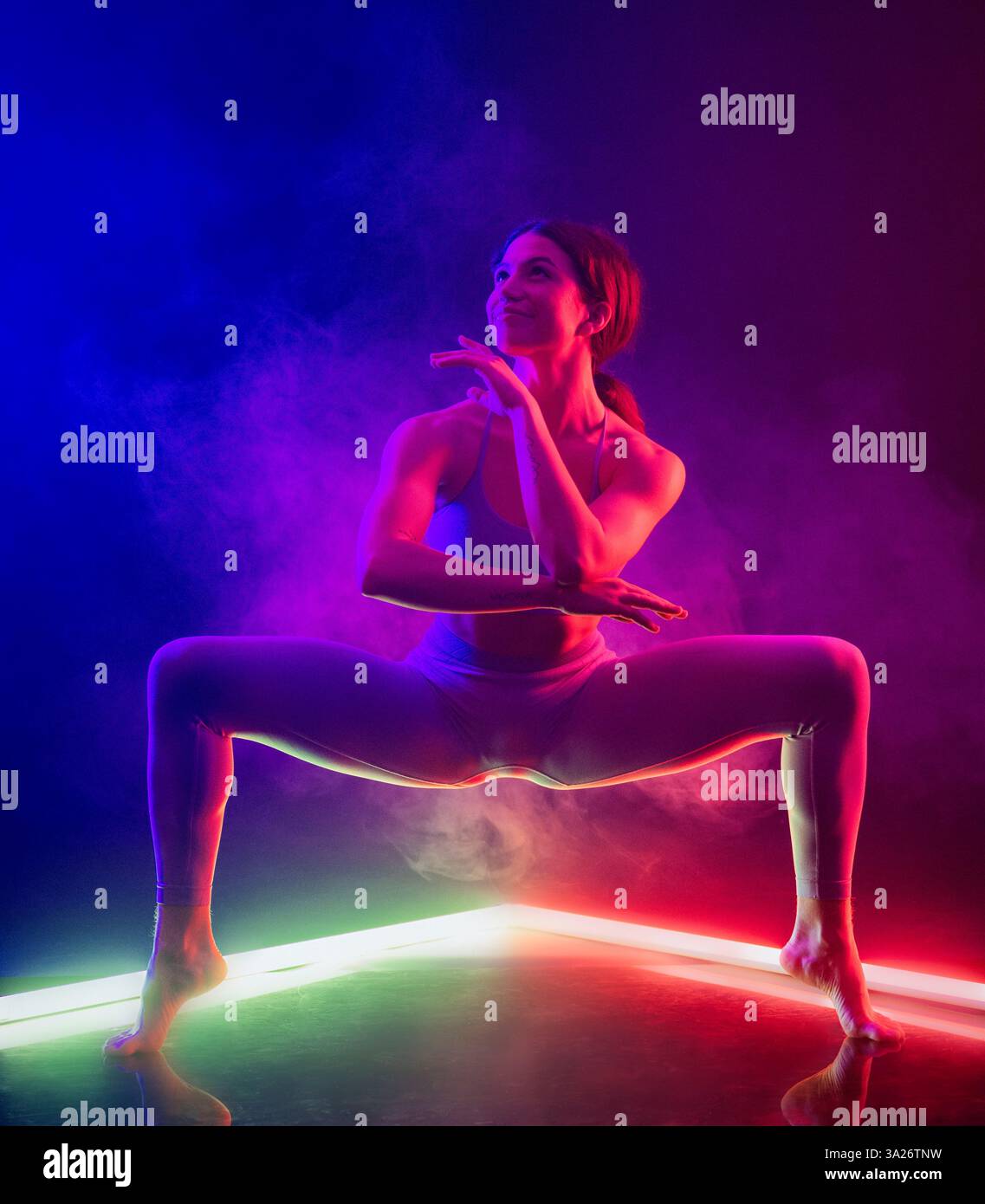 Frau in Tanzposition mit dramatischem Neonrot und Blau, umgeben von Nebel. Stockfoto
