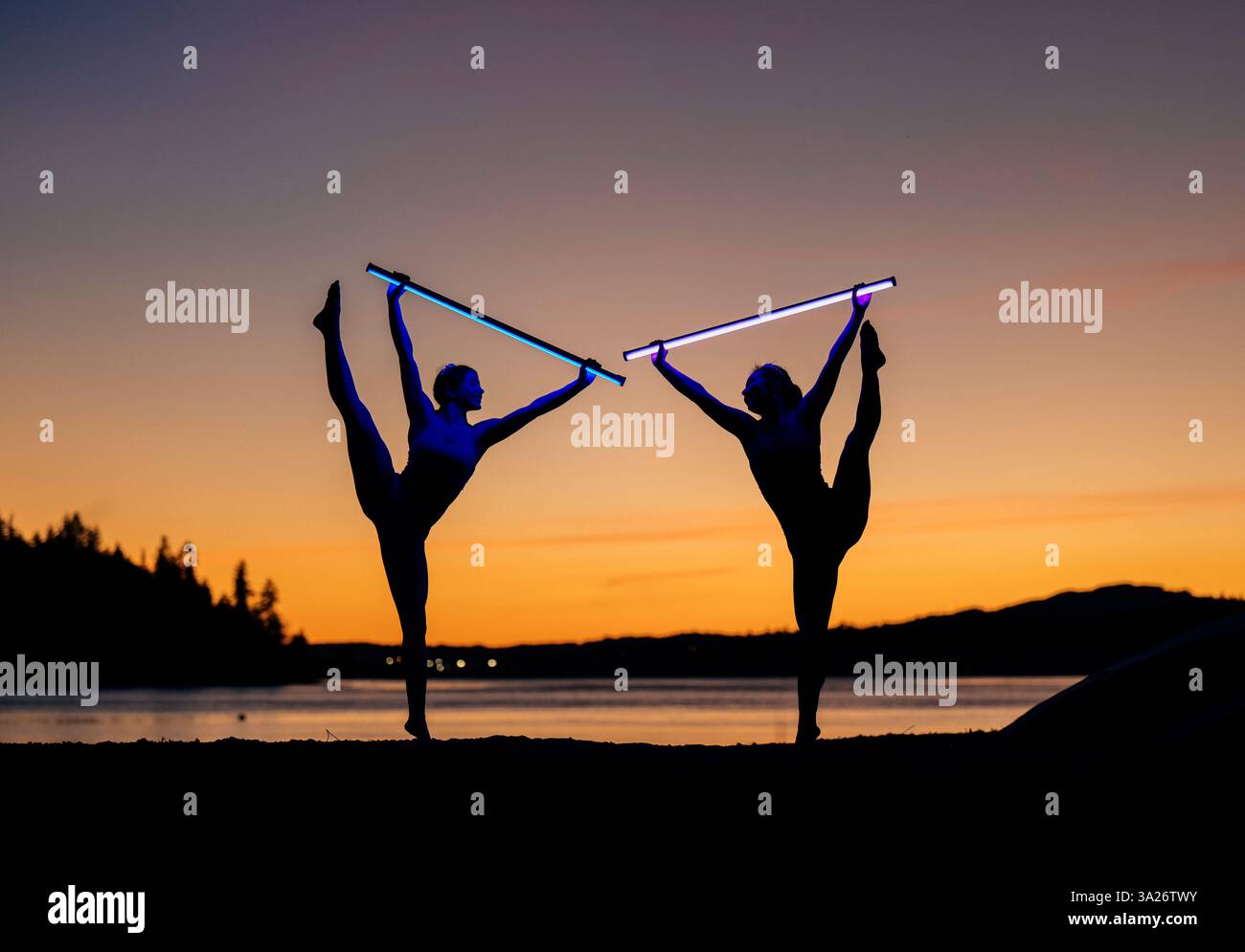 Zwei Tänzer treten bei Sonnenuntergang mit leichten Säbeln an einem See auf, die sich vor dem farbenfrohen Himmel bilden. Bainbridge Island, WA, USA Stockfoto