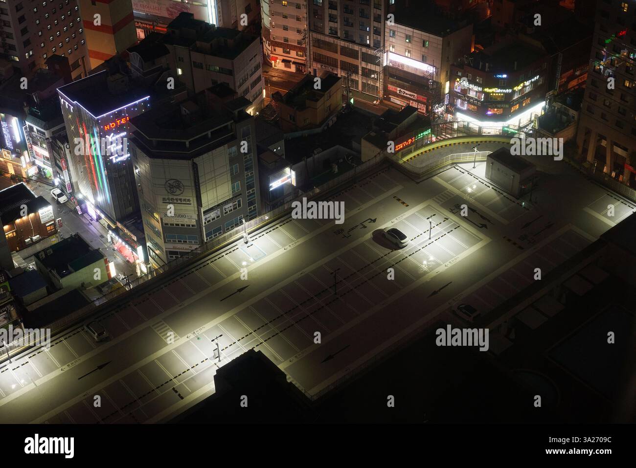 Beleuchteter städtischer Parkplatz auf dem Dach, umgeben von hohen Gebäuden bei Nacht in einer belebten Stadt. Busan, Korea Stockfoto