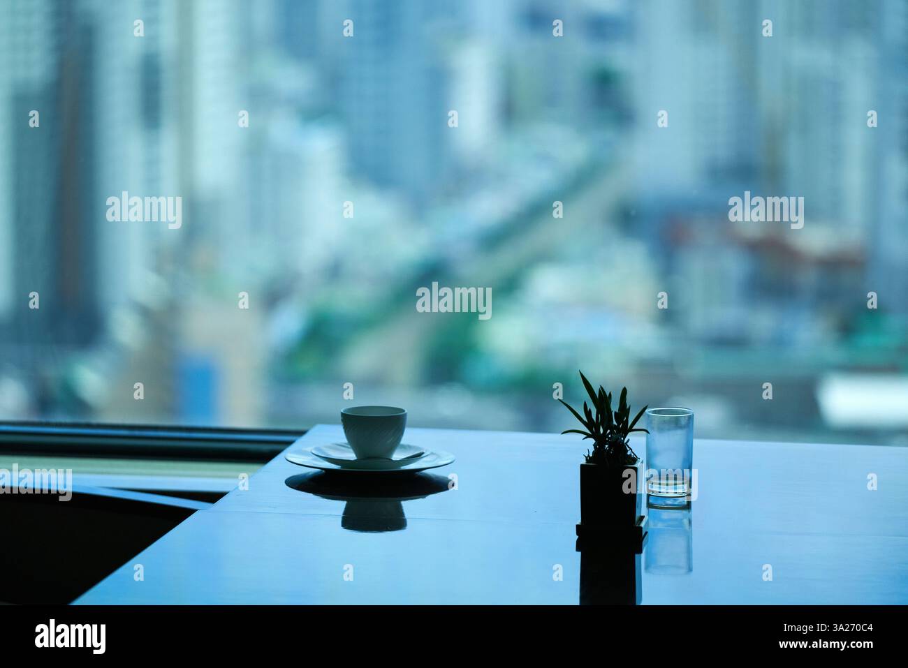 Ein Tisch in einem Hotelzimmer mit Tasse, Glas und kleiner Pflanze vor einem verschwommenen Stadtbild. Busan, Korea Stockfoto