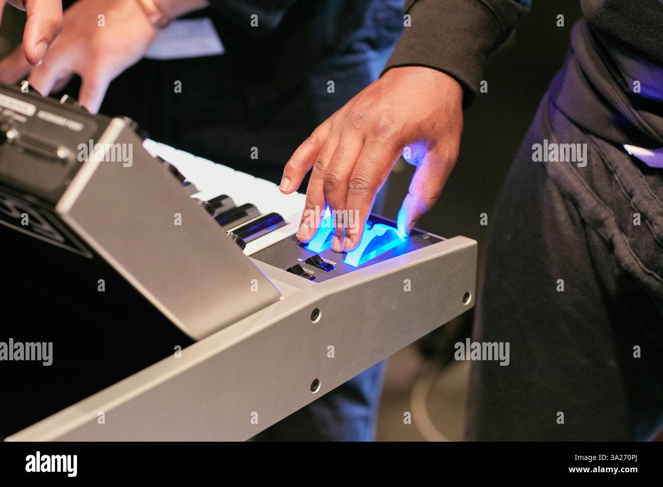 Nahaufnahme von Händen, die auf einer elektronischen Tastatur mit einer blau beleuchteten Taste spielen. Stockfoto